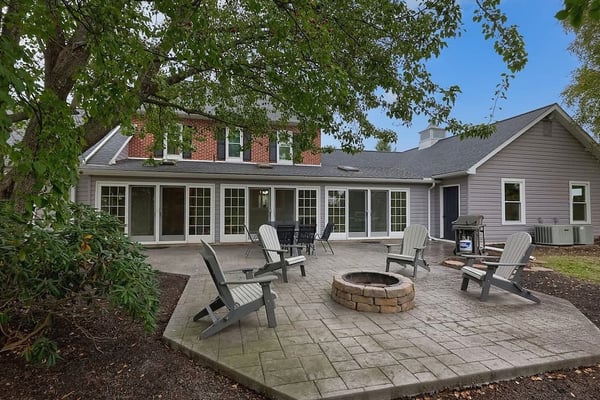 Modern black cabin with wooden porch nestled among tall trees, gravel patio with Adirondack chairs, wooden deck railing in foreground.